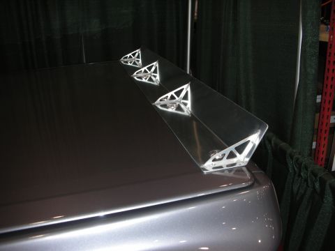 1998 Ford Crown Victoria - custom chrome spoiler with triangular skeletal supports is mounted on a silver car's trunk lid against a dark curtain.