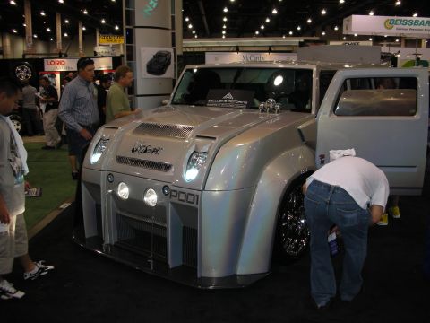 1998 Ford Crown Victoria - silver custom concept vehicle with rounded fenders and round headlights sits under spotlights at a crowded automotive trade show.