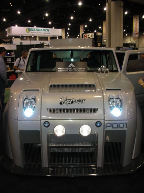 1998 Ford Crown Victoria - Front view of a silver custom vehicle showing twin round driving lights, illuminated headlights and a 'P001' badge under exhibition lightin…