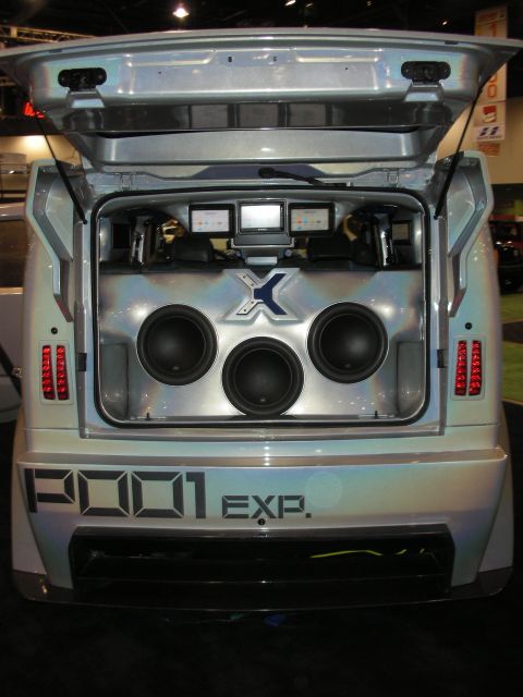1998 Ford Crown Victoria - open rear hatch of a silver 'P001 EXP' custom vehicle reveals a trunk audio install with three subwoofers and amplifiers.