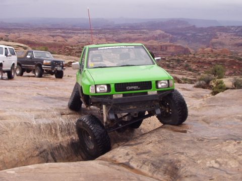 1993 Ford Bronco - This modified green SUV is tackling a challenging off-road course in a desert landscape.