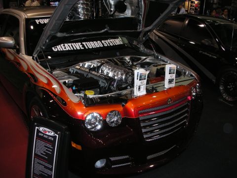 1998 Ford Crown Victoria - Dodge sedan with flame-painted fenders shows its chromed engine bay under a 'Creative Turbo Systems' banner at a show.