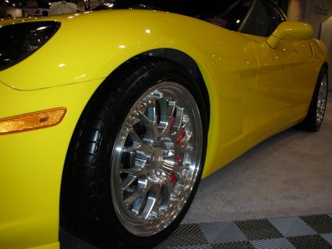1998 Ford Crown Victoria - Close-up of a yellow Corvette's front wheel arch showing a polished multi-spoke wheel and red brake caliper.