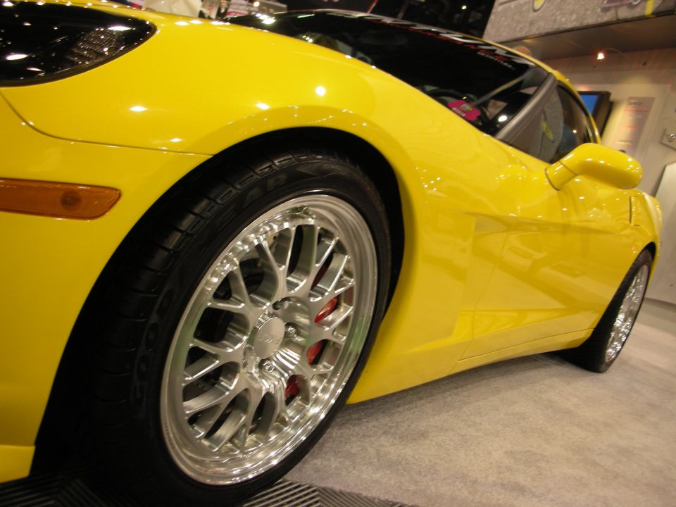 Front wheel of yellow Corvette with polished mesh wheel and red caliper