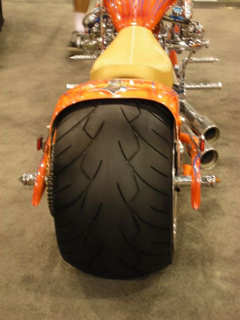 1998 Ford Crown Victoria - Rear view of an orange flame-painted custom chopper motorcycle showing its fat rear tire, dual exhausts and tan seat.