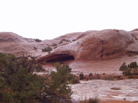 1993 Ford Bronco - A vast desert scene unfolds with towering red rock formations and a prominent cave entrance, under a bright sky.