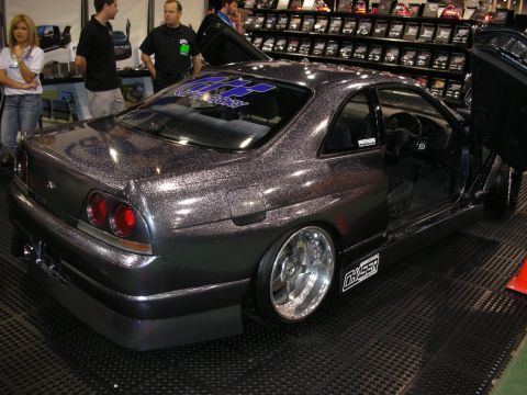 1998 Ford Crown Victoria - Rear three-quarter view of a metallic-flake Nissan Skyline coupe with a body kit and deep-dish chrome wheels at a tuning show.