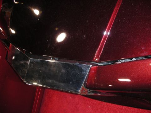 1998 Ford Crown Victoria - Close-up of a deep-red metallic-flake body panel meeting a chrome trim piece, photographed over red show-floor carpet.