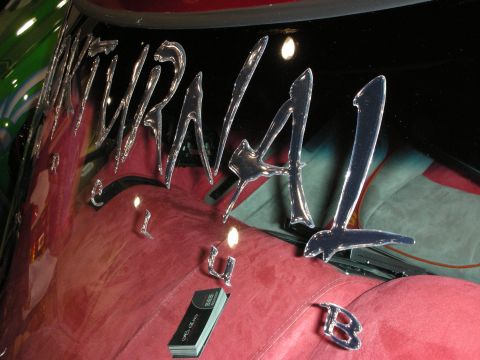 1998 Ford Crown Victoria - Polished chrome script reading part of a name mounted on a glossy black panel above red velour upholstery in a custom show car.