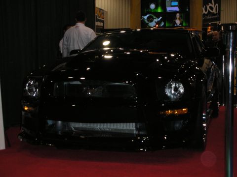 1998 Ford Crown Victoria - glossy black modified coupe with custom front fascia and intercooler photographed front-on under dim convention lighting.