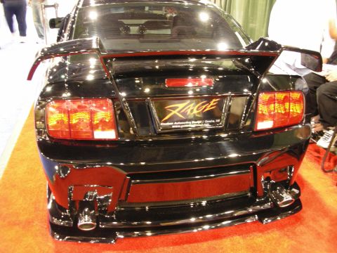 1998 Ford Crown Victoria - Rear view of a black custom coupe with a wing, twin tips, custom taillights and a 'RAGE' decal at an indoor show booth.