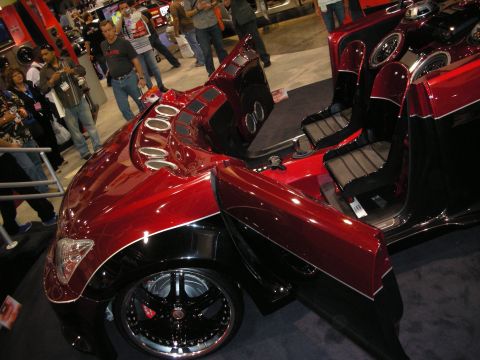 1998 Ford Crown Victoria - High-angle view of a candy-red custom car with an open door and chrome-ringed speaker pods, surrounded by show spectators.