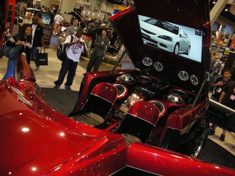 1998 Ford Crown Victoria - Candy-red custom show car with raised hatch revealing a ringed-speaker install and an integrated video screen at a trade show.