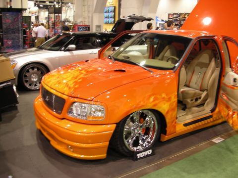 1998 Ford Crown Victoria - orange flame-airbrushed lowered pickup with chrome wheels and an open door revealing a custom tan interior at an indoor show.