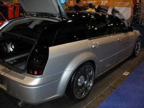 1998 Ford Crown Victoria - silver custom station wagon with black roof, large chrome wheels and an open hatch showing an audio install at a trade show.