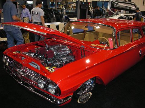 1998 Ford Crown Victoria - red early-1960s custom station wagon with hood up revealing a polished chrome engine, displayed at an indoor car show.