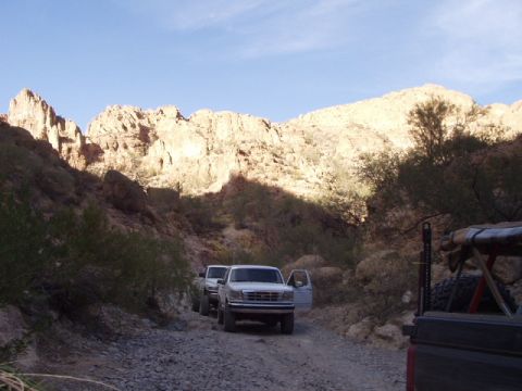 1993 Ford Bronco - Two trucks drive down a rocky canyon road with mountains in the background.