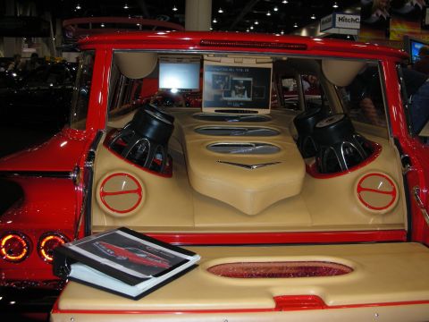 1998 Ford Crown Victoria - show vehicle's tan-upholstered rear cargo area packed with two subwoofers, a video screen and a brochure resting on the tailgate.