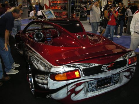1998 Ford Crown Victoria - rear of a dark-red custom sports car with airbrushed silver flame graphics, an SCZ Sound badge and rear-deck speakers at a show.
