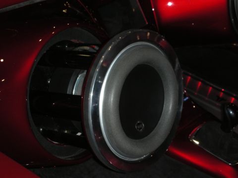 1998 Ford Crown Victoria - close-up of a large chrome-rimmed subwoofer set into the glossy candy-red panel of a custom car.
