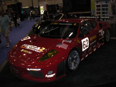 1998 Ford Crown Victoria - red Ferrari race car numbered 62 in Forza Motorsport 2 livery displayed on a stand at an indoor show.