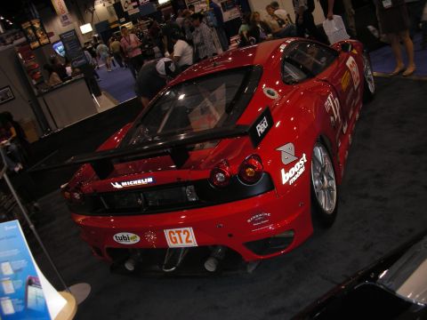 1998 Ford Crown Victoria - rear three-quarter view of a red Ferrari F430 GT2 race car with a large rear wing and sponsor decals on a carpeted show floor.