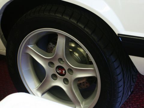 2001 Mercury Grand Marquis - Close-up of a silver five-spoke wheel with a red emblem, mounted on a white vehicle.