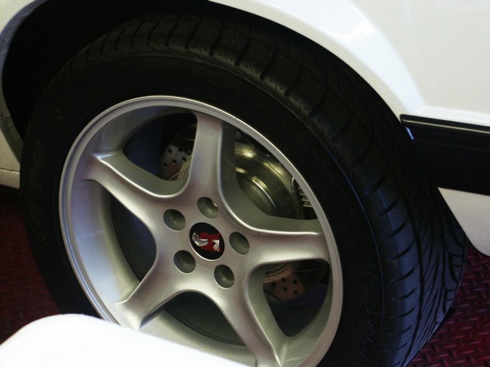 Silver five-spoke wheel with a red emblem on a white car