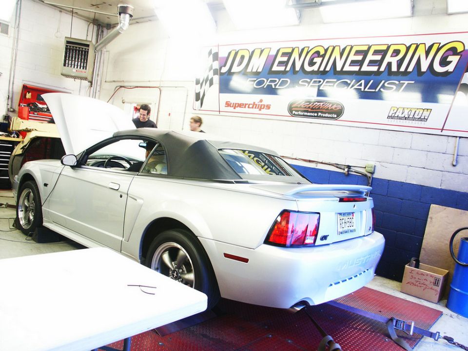 Silver convertible sports car on a dynamometer in a garage with 'JDM ENGINEERING' banner
