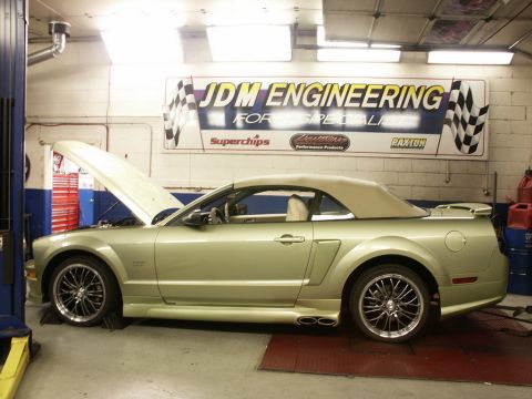 2001 Mercury Grand Marquis - A convertible Mustang is positioned on a lift inside a garage, with its hood open and a prominent JDM Engineering banner overhead.