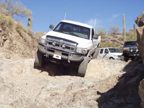 1993 Ford Bronco - A white 1994 Dodge Ram pickup truck tackles a challenging off-road trail with other vehicles visible in the background.