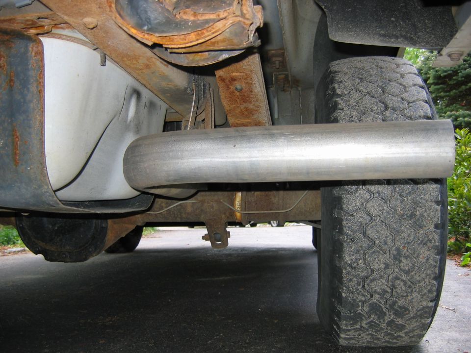 New stainless exhaust pipe routed under a vehicle near rear tire