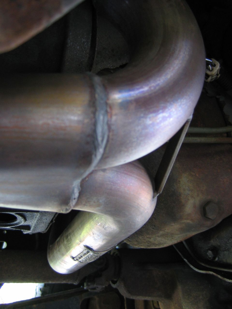 Close-up of stainless steel exhaust headers with weld seams under a vehicle