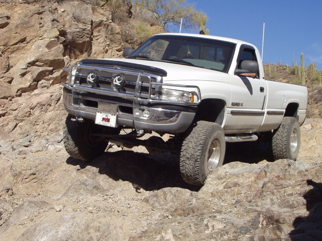 White Dodge Ram pickup with grille guard crawling down a rocky desert trail among saguaro cacti