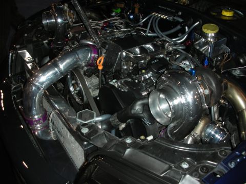 1998 Ford Crown Victoria - highly polished twin-turbo engine bay with chrome charge piping, coolant reservoirs and a carbon-fiber trim panel in a dark car.