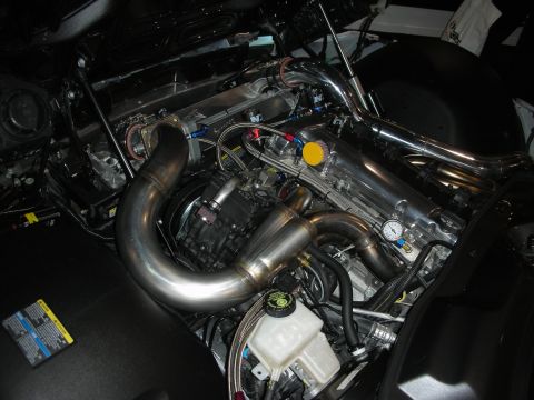 1998 Ford Crown Victoria - polished stainless turbo header and looping charge pipe with a boost gauge in a dark, detailed engine compartment.