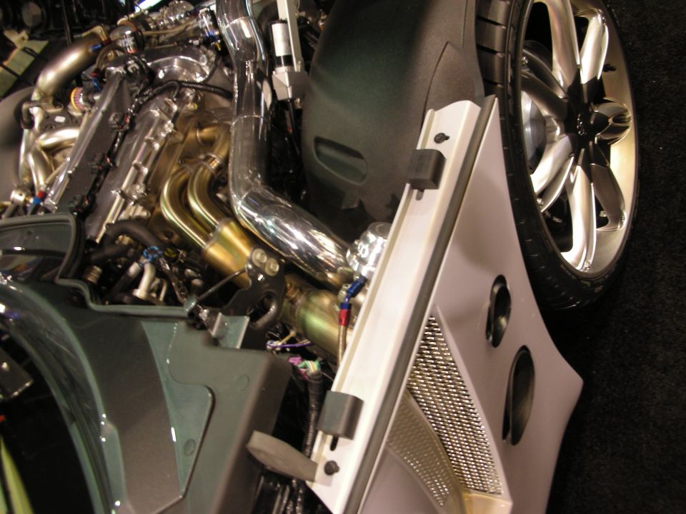 Polished engine and tube headers above chrome wheel on green show car