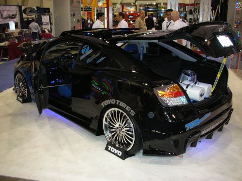 1998 Ford Crown Victoria - black tuner coupe with open doors, ground-effects body kit, chrome wheels and Toyo Tires placards on a carpeted show stand.