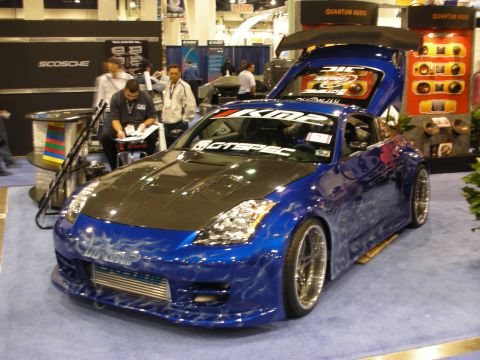1998 Ford Crown Victoria - blue Nissan 350Z show car with a carbon-fiber hood, wide body kit, flame paint and KMC and DC Sports decals on a show floor.