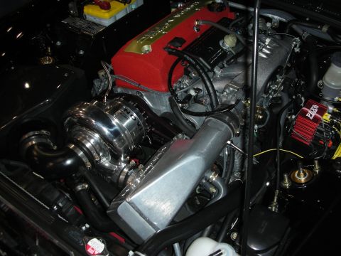 1998 Ford Crown Victoria - close-up of a polished chrome supercharger or turbo mounted beside a red engine cover, with braided lines and an aluminum reservoir.