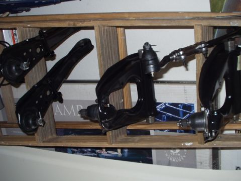 Black suspension control arms and ball joints on a wooden shelf