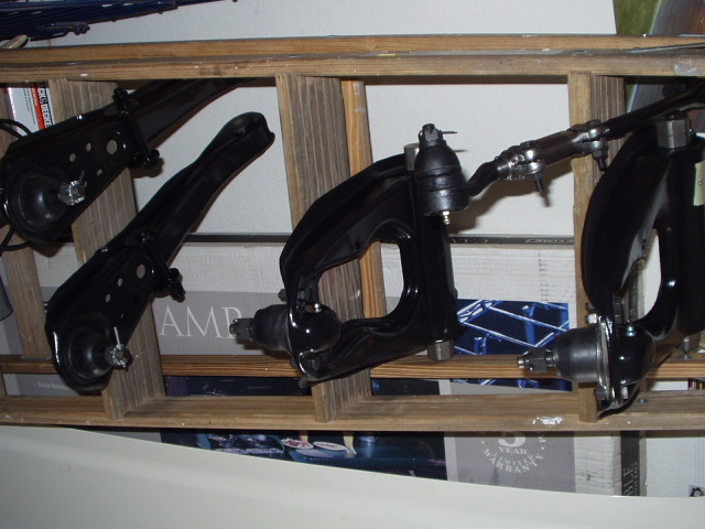 Black suspension control arms and ball joints on a wooden shelf