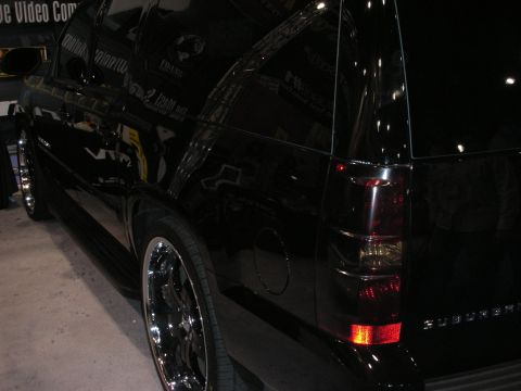 1998 Ford Crown Victoria - dark rear quarter of a black full-size SUV with chrome wheels and tinted tail lights is shown at an indoor display.