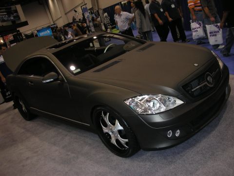 1998 Ford Crown Victoria - matte-grey Mercedes-Benz coupe with a custom grille badge and chrome multi-spoke wheels sits on display as crowds walk past.