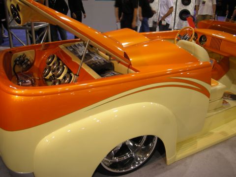 1998 Ford Crown Victoria - two-tone orange-and-cream custom hot rod truck with pinstriping, chrome wheels and an open engine bay full of audio speakers.