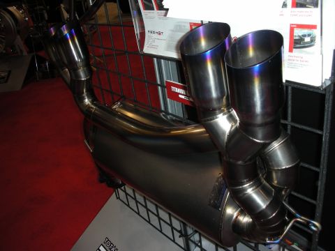 1998 Ford Crown Victoria - titanium exhaust system with twin burnt-blue tailpipe tips is displayed on red carpet at a vendor booth.