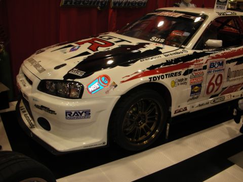 1998 Ford Crown Victoria - white Nissan Skyline GT-R race car covered in sponsor decals and numbered 69 sits on display at an indoor show.