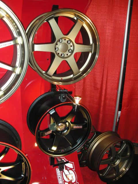 1998 Ford Crown Victoria - Several bronze and black six-spoke wheels are mounted against a red curtain at a vendor display booth.