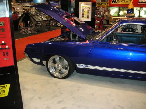 1998 Ford Crown Victoria - blue side profile of a custom muscle car with raised hood, white side stripe and polished five-spoke wheels at a show.