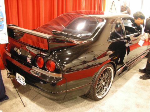 1998 Ford Crown Victoria - black Nissan Skyline GT-R coupe shows its rear three-quarter and GT-R badging on an indoor show floor.